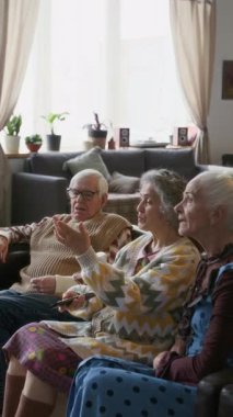 Oturma odasındaki kanepede oturup uzaktan kumandayla emekliler yurdunda hangi televizyon programını izleyeceklerini tartışan yaşlı arkadaşların dikey görüntüleri.