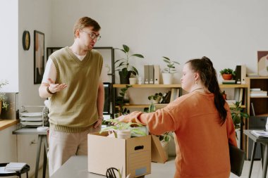 Dost canlısı bir erkek ofis çalışanı, yeni kadın iş arkadaşıyla sohbet ederken çekilmiş. Down sendromlu. Karton kutusunu açıyor.