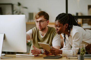 Ofiste birlikte uygulama geliştirirken Afrikalı Amerikalı ve Kafkas geliştiricilerin bilgisayar monitörlerine dikkatlice baktıkları orta boy bir fotoğraf.