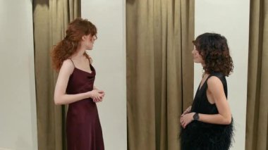 İki kız yeni giysiler içinde nasıl göründüklerini tartışıyor soyunma odasından çıkıp etrafında dönen arkadaşlarını bekliyorlar, sonra da genç kadınlar heyecanla elbisesini inceliyorlar.