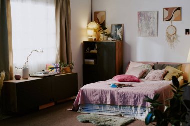 Yastıklı çift kişilik yatak, koyu ahşap şifonyer ve üstünde süslemeler olan klozet.