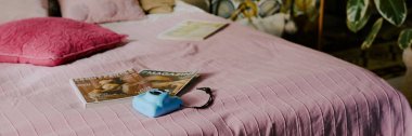 Üzerinde pembe battaniye ve turkuaz hazır kamera ve dergiler olan çift kişilik yatak sitesi afişi.