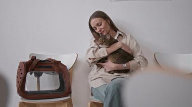 Bekleme odasında evcil hayvan taşıyıcısının yanında oturan bir kadın veteriner kliniğinde muayeneden önce kedisini teselli ediyor.