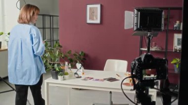 Profesyonel stüdyoda video kaydetmeden önce masasına oturup saçını ve makyajını yapan bir kadın.