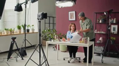 Film yönetmeni aktrisle senaryo tartışıyor, profesyonel stüdyoda video kaydına hazırlanıyor.