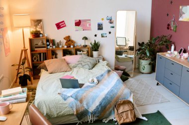 Ahşap raflar, modern mobilyalar ve çeşitli dekorasyon unsurlarından oluşan düzenli bir alan. Kişisel dokunuşlar ve doğal ışıklandırma ile samimi ve davetkar bir yatak odası ortamı yaratıyor.