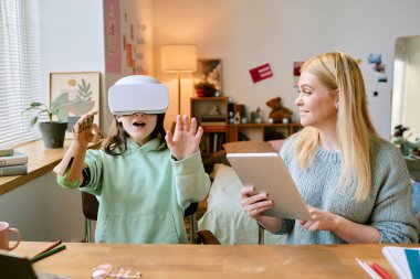 Sanal gerçekliğe dalmış protez elli bir çocuk, elinde tablet tebessümleri, oyuncaklar ve sanatla süslenmiş bir şekilde oturma odasında beklerken merakla karşılaşıyor.