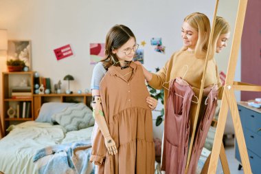 Sarışın anne ve esmer genç kız protez kollu çekici elbiseyi inceliyor güzelce dekore edilmiş rahat bir yatak odasında gülümserken.