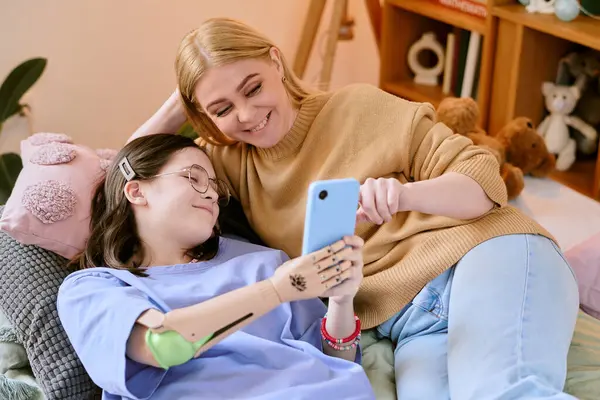 Genç kızıyla kanepeye yaslanmış gülümseyen bir kadın protez eliyle ona akıllı telefon dostu bir anda bir şey gösteriyor.