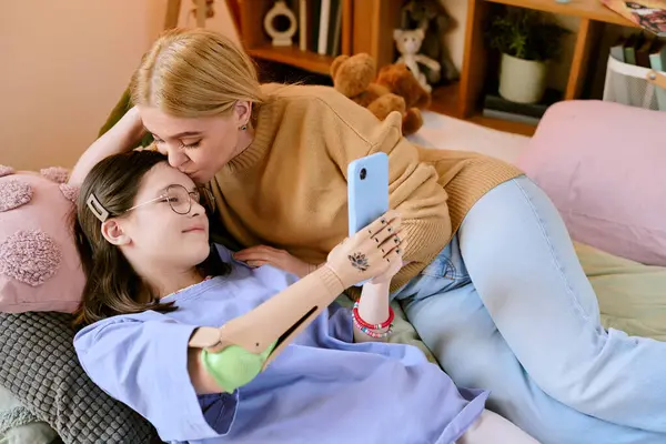 Sevgili annesi onu alnından öperken ve şefkatli bir anı yakalarken protez kollu mutlu bir kız selfie çekiyor.