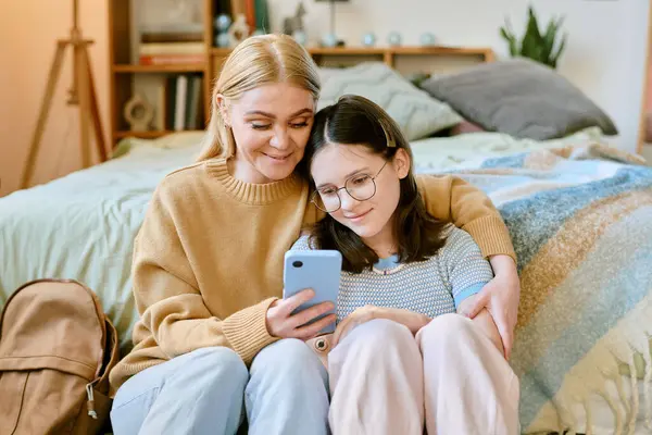 Kadın ve çocuk yerde oturuyor, akıllı telefona gülümsüyorlar. Yumuşak battaniyeli ve yastıklı rahat yatak odası seti, her ikisi de gündelik kıyafetler giyiyor.