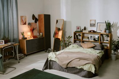 Güneş ışığı, rahat bir yatak odasını nazikçe aydınlatıyor. Temiz bir yatak odası, ahşap mobilyalar ve iç mekan bitkileri gibi doğal dekorasyon unsurları var. Huzurlu ve davetkar bir atmosfer yaratıyor.