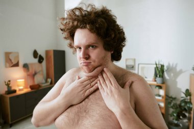 Modern bir oturma odasında modern mobilyalar ve ev bitkileriyle süslenmiş göğsüne dokunan kıvırcık saçlı bir adamın portresi.