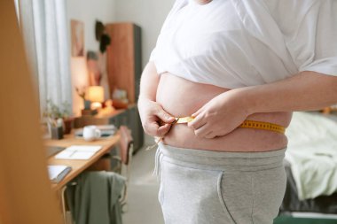 Modern yatak odasındaki kemeri ayarlayan kişi, arka planda masa ve ayna ile rahat ve kişisel bir atmosfer yaratarak refah ve zindelik üzerine odaklanıyor.