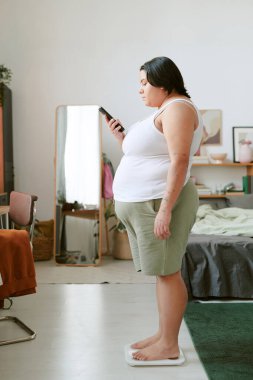 Güzel dekore edilmiş bir odada terazide, rahat mobilyalar ve dekorla ayakta duran bir kadın. Portre aynaları ve resim çerçevesi sahne