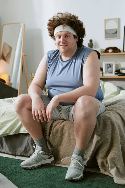 Rahat yatak odasındaki kanepede rahat rahat giyinen biri. Yatak ve duvar dekoru arka planda görünür, rahat atmosfere eklenir