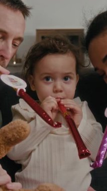 Çeşitli genç çiftlerin ve bebek kızlarının doğum günü partilerinde düdük çalmalarına dikey bir bakış açısı.