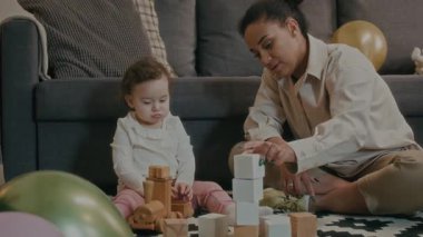 Genç anne ahşap küpleri inşa ediyor ve küçük kız oturma odasında yerde oynarken onu yok ediyor.