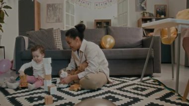 Genç bir anne oyuncak tutarak kızını ahşap trenle oynarken seyrediyor, sonra da oturma odasında onun fotoğrafını çekiyor.