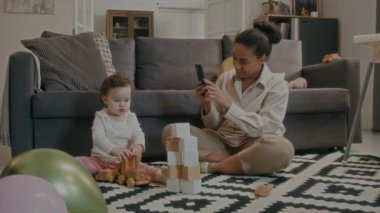 Genç bir kızın tahta trenle oynadığı videoyu kaydediyor ve halının üzerinde gri kanepe arkasında otururken bir yandan da küp yığınını yok ediyor.