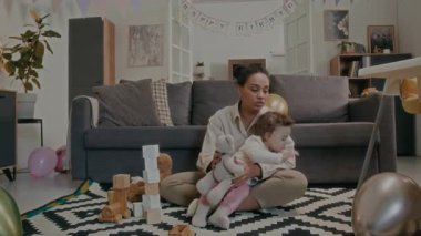 Genç anne, bebek kızına dikkat etmeye çalışıyor ve onunla iletişim kuruyor. Kız, oturma odasında halının üzerinde otururken oyuncaklarla oynamayı reddediyor.