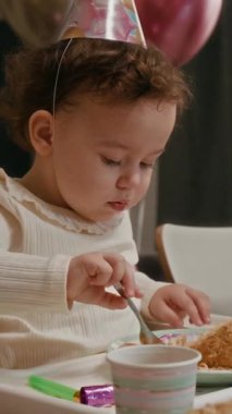 Doğumgününün tadını ebeveynleriyle birlikte çıkaran küçük kızına bir parça kek ayıran annenin dikey görüntüsü.