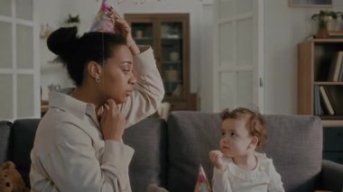 Mutlu anne evde doğum gününü kutlarken kendine, küçük kızına ve oyuncak hayvanına parti şapkası takıyor.