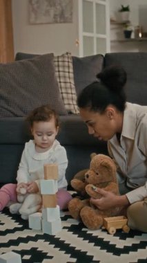 Oturma odasında otururken pelüş oyuncaklar ve tahta küplerle oynayan küçük anne ve kız çocuğunun dikey görüntüsü