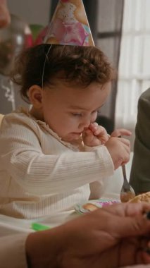 Küçük kızın parti şapkası taktığı, annesiyle doğum günü pastası yediği ve evde bayram yemeği yerken tanınmayan babasının dikey görüntüsü.