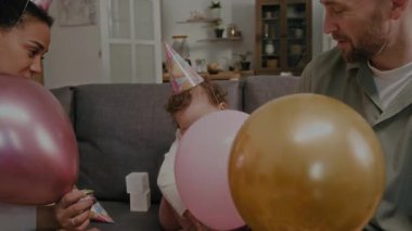 Çok ırklı ebeveynler ve küçük kız bebeklerin doğum günü partisi sırasında balonlarla iletişim kurup oynuyorlar.