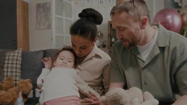 Annesinin kollarında kıvranan yorgun bir kız bebek. Pozitif baba evde doğum günü partisinde dikkatini doldurulmuş oyuncaklara çevirmeye çalışıyor.