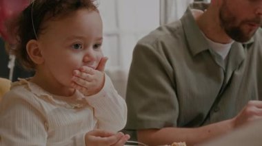 Evli çift ve parti şapkalı bebekleri evde doğum günü kutlaması sırasında pasta yiyorlar.