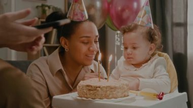 Neşeli baba, eşiyle ve elleriyle pasta yiyen küçük kızıyla fotoğraf çekiyor. Yemek sandalyesinde oturuyor, sonra da aile mumları birlikte üflüyor.