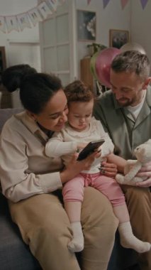 Farklı eşlerin ve küçük kızın doğum günü partisinde koltukta otururken akıllı telefon kullanması, babasının yumuşak oyuncaklar tutması.