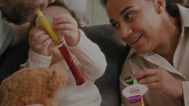 Sevgi dolu ebeveynlerin ve küçük kızın evde kızların doğum günlerini kutlarken onlarla oynayıp ıslık çaldığı yakın plan görüntüsü.