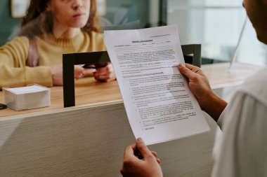 Ofis ortamında müşteri ile iletişim kurarken elinde belge tutan erkek, arka planda talimat bekleyen ve işlem bekleyen kadın