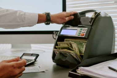 Modern ofis ortamında elektronik bir makineyle nakit saymak, para faturaları görünür, makineyi elle çalıştırmak, finansal görevlere ve doğruluğa odaklanmak
