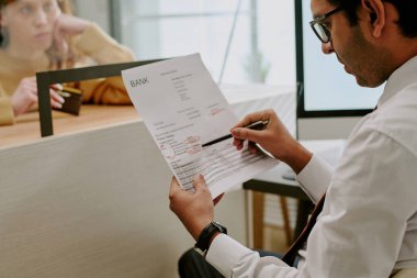 Banka çalışanlarıyla ofis atmosferinde banka tezgahında evrak imzalayan adam, mali konuları ve evrak işlerini tartışıyor, iş resmi kıyafetlerle profesyonel çevre