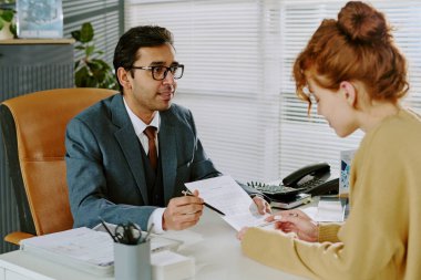 Takım elbiseli bir işadamı, modern ofis masası, ofis bitkileri ve modern dekorasyonda çalışan kadın meslektaşıyla birlikte belgeleri inceliyor. Rahat, profesyonel bir ortam yaratıyor.