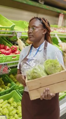 Hipermarkette çalışan genç Afrikalı Amerikalı tezgahtarın taze marul sererken dikey görüntüsü.