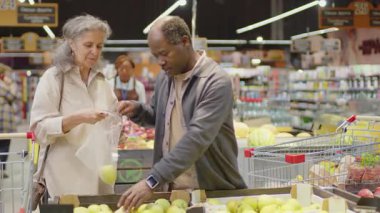 Orta boy Afrika kökenli Amerikalı bir adam ve beyaz karısının modern süpermarkette alışveriş yaparken elma toplarken çekilmiş bir fotoğrafı. Duvarda 