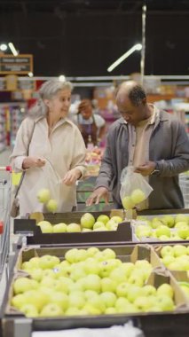 Mutluluk dolu yaşlı karı ve koca süpermarkette yiyecek alırken elma seçerken orta boy dikey çekim.
