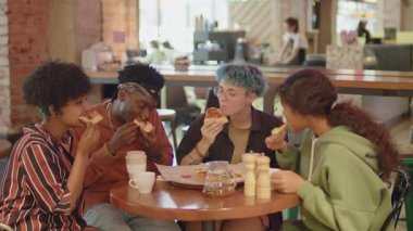 Kafe masasında oturan, lezzetli pizzalar yiyen ve sohbet eden çok ırklı Z jenerasyonundan arkadaşlar.