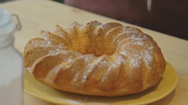 Mutfak masasında servis edilen taze pişmiş Meskouta kekinin tozunu alırken yakın çekim.