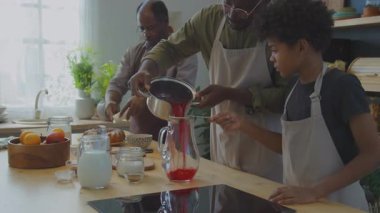 Afrika kökenli Amerikalı baba ve küçük oğlu Zobo çayını cam sürahiye süzüyorlar. Büyükbabaları ev yemeği için geleneksel yemekleri hazırlarken Meskouta keki servis ediyor.