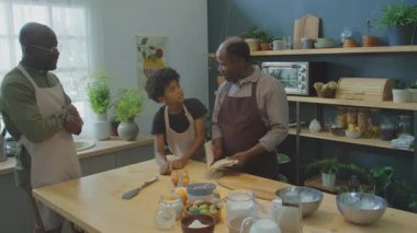 Afrika kökenli Amerikalı büyükbaba yemek kitabında aile tarifini okurken baba da evde yemek pişirmeden önce mutfakta onlara katılıyor.