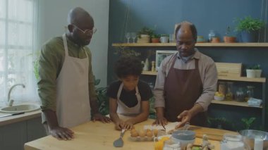 Orta boy Afrika kökenli Amerikalı büyükbaba yemek kitabı okurken ve mutfakta yemek yapmaya hazırlanırken gizli aile tarifini oğluyla ve torunuyla paylaşırken.