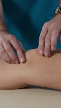 Tanımlanamayan rehabilitasyon uzmanının elleri dikey yakın çekim. İş günü, kimliği belirsiz bir kızın dizini muayene ediyor.