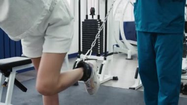 Yanında duran erkek rehabilitasyon uzmanının kontrolü altında çalışan kimliği belirsiz genç bir kadın.