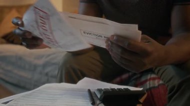 Orta yaşlı Afro-Amerikan bir adamın, vadesi geçmiş faturaları ve tahliye ihtarı hakkında endişeli bir görüntüsü.